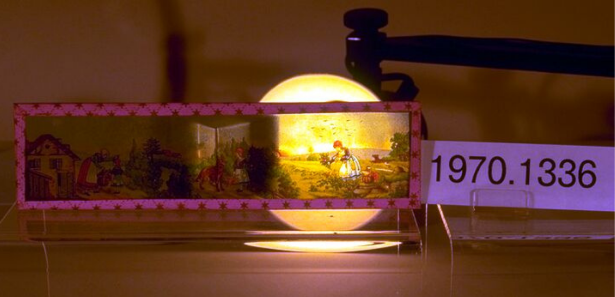 A magic lantern; a light illuminates a scene of a woman picking flowers